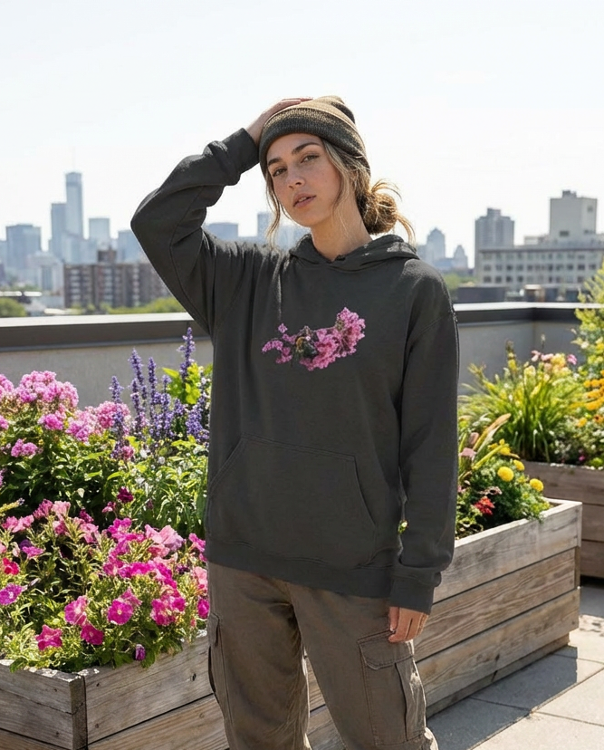 Person wearing a hoodie with floral design on a rooftop with city skyline and flowers in the background